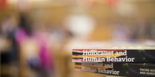 Two Holocaust and Human Behavior books are stacked on a table and the background is blurred out.