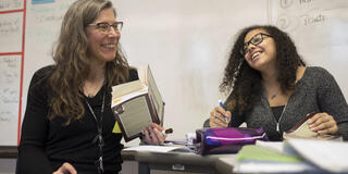 An ELA teacher and student laugh as they discuss a book.