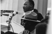 Dr. Martin Luther King, Jr. stands at a microphone giving a speech to a crowd.