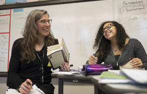 An ELA teacher and student laugh as they discuss a book.