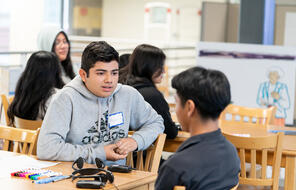 students sitting at a table talking with headphones on the table