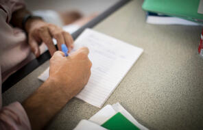 person holding a blue pen and writing on a sheet of paper