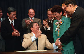 President Ronald Reagan celebrates with senators and representatives during a signing ceremony in the Old Executive Office Building in Washington on Aug. 10, 1988.