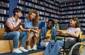 Diverse group of students in college library including young woman in wheelchair enjoying discussion.