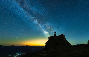 a person standing on a mountain with the sun setting against the blue night sky