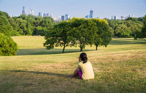 person sitting in a park looking at the city skyline wearing pink shorts and a yellow shirt and their hair is in a pony tail 