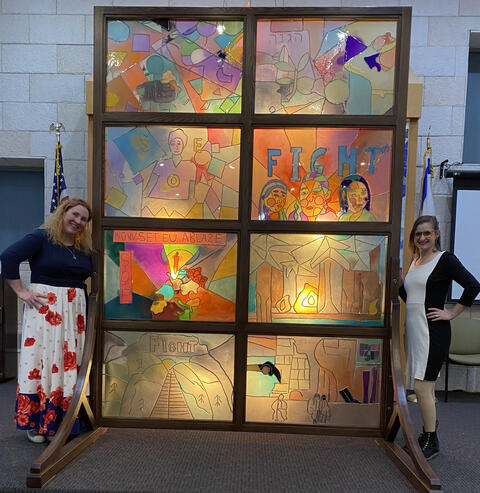 Two educators stand in front of a stained glass window.