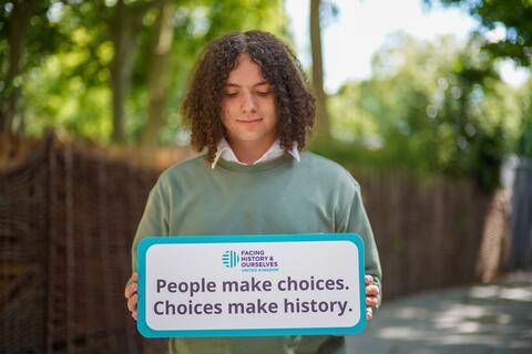 Student holds "People make choices. Choices make history." sign. 