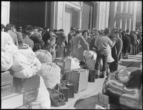 With baggage stacked, residents of Japanese ancestry await bus at Wartime Civil Control Administration station, 2020 Van Ness Avenue, as part of the first group of 664 to be evacuated from San Francisco on April 6, 1942. Evacuees will be housed in War Relocation Authority centers for the duration.