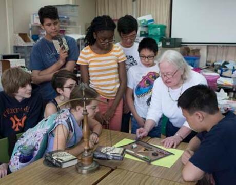 A teacher speaks to a group of students gathered around them at a table