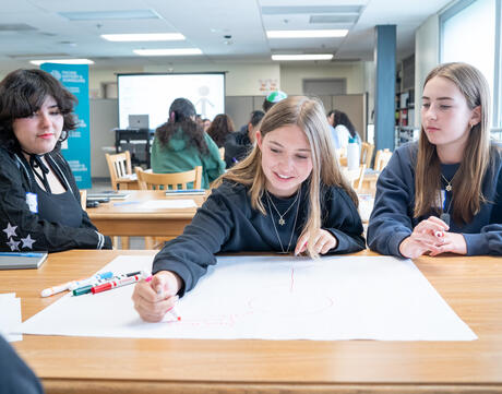 A group of three students at a table collaborating on a poster paper