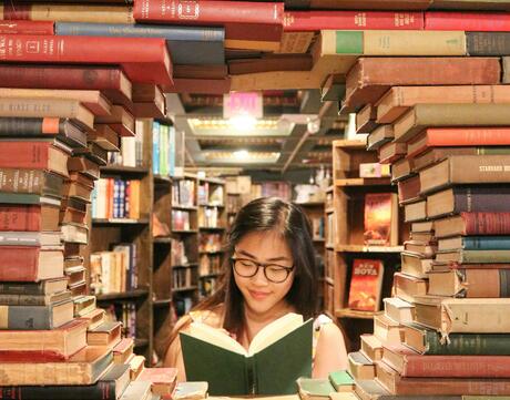 Asian American teen surrounded by creatively stacked library books