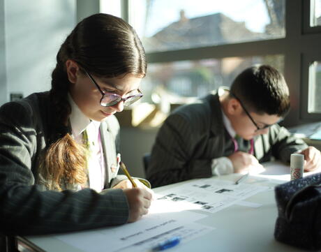 Two students seated at a desk work on handouts.